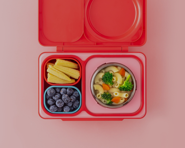 Pink and red OmieBox UP with pasta, blueberries and baby corn on a blush tabletop.