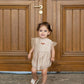 Child wearing the pale rose Donsje Vailen playsuit in front of wooden doors.