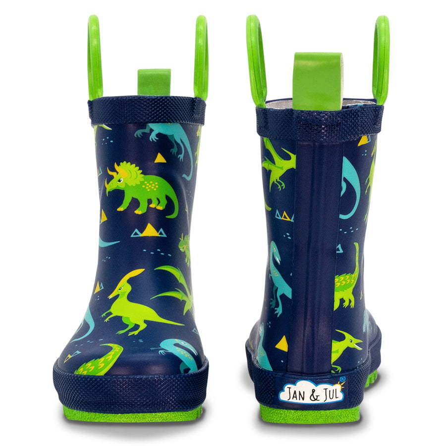 Navy Jan & Jul rain boots with colorful dinosaur illustrations and green pull handles.