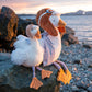 Two aviator-themed plush birds posed together beside the sea.