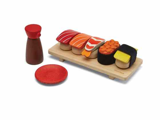 PlanToys pretend sushi arranged on a wooden tray beside a red plate and sauce bottle.