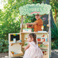 Two children playing at the Woodland Stores toy shop outdoors beneath a tree.
