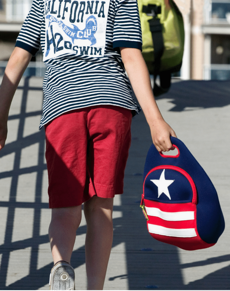 Child carrying a navy Dabbawalla Stars & Stripes lunch bag with red-and-white stripes.
